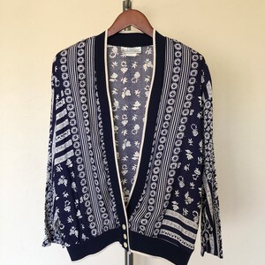 May include: A navy blue cardigan with a white floral pattern. The cardigan has a V-neck and a button closure. The label reads "Ellen Tracy".