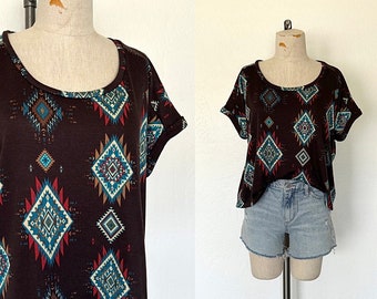May include: A brown, cropped, short-sleeved shirt with a geometric pattern in shades of blue, red, and white. The shirt has a scoop neck and a relaxed fit.