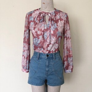 May include: A pink and blue floral print blouse with a tie at the neck, worn with high-waisted denim shorts.