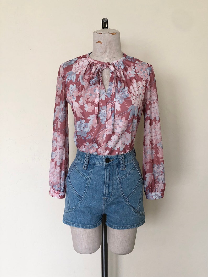 May include: A pink and blue floral print blouse with a tie at the neck, worn with high-waisted denim shorts.
