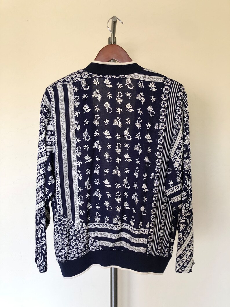 May include: A navy blue long-sleeved cardigan with a white floral pattern. The cardigan is made of a soft, lightweight fabric and has a relaxed fit.
