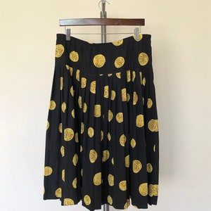 Op de afbeelding: Een zwarte geplooide rok met een gouden muntprint. De rok is midi-lang en heeft een ontspannen pasvorm.