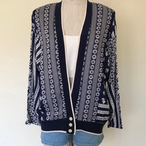 May include: A navy blue cardigan with a white and cream patterned design. The cardigan has a button closure and long sleeves.