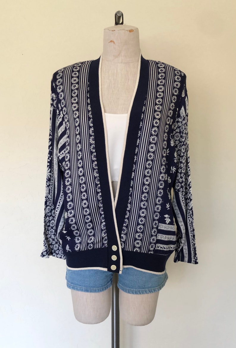 May include: A navy blue cardigan with a white and cream patterned design. The cardigan has a button closure and long sleeves.