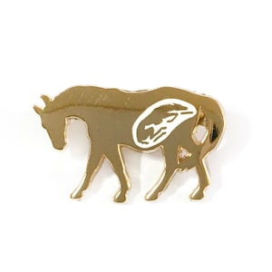 May include: Gold-coloured metal pin shaped like a horse. The horse is walking and has a white outline of a horse's head on its side.