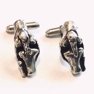 May include: A pair of silver cufflinks with a detailed, abstract design. The cufflinks are made of metal and have a polished finish.