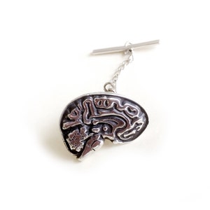 May include: A silver tie tack featuring a detailed anatomical model of a human brain.