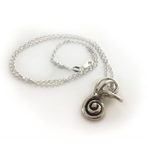 May include: A silver necklace with a detailed, abstract pendant shaped like a spiral. The pendant is attached to a delicate silver chain.