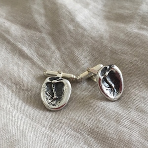 Può includere: Un paio di gemelli d'argento con un design unico. Ogni gemello presenta un'impronta dettagliata di un'impronta di mano.