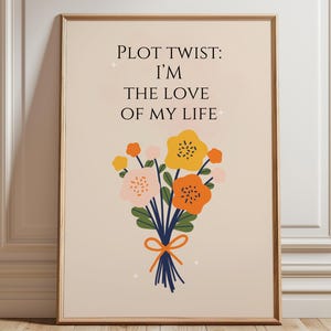 Pode incluir: Uma impressão artística emoldurada com o texto "PLOT TWIST: I'M THE LOVE OF MY LIFE" acima de um buquê de flores. O buquê apresenta flores amarelas, laranja e rosa amarradas com uma fita azul. O fundo é bege claro.