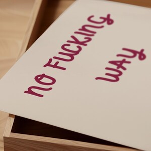 May include: A rectangular, off-white print with the words "NO FUCKING WAY" in a handwritten, dark pink font. The print is inside a wooden box, partially visible in the image.
