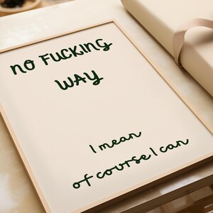 May include: A framed print with the text "no fucking way" in dark green cursive. Below, the text continues with "I mean of course I can". The frame is a light wood color, and the background is a cream color.