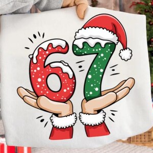 May include: A white Christmas-themed graphic featuring the numbers 67, each held by a pair of hands. The number 6 is red with white accents, and the number 7 is green, both with Santa hats. The design is festive and celebratory.