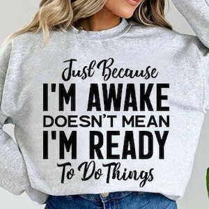 Puede incluir: Sudadera gris claro con el texto negro: "Just Because I'm Awake Doesn't Mean I'm Ready To Do Things". La parte superior informal es adecuada para el uso diario.