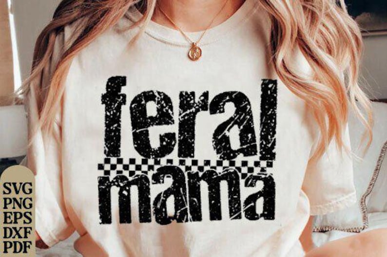 May include: Cream-colored t-shirt with the words "feral mama" in distressed black lettering. The word "feral" is above "mama", separated by a black and white checkered pattern. A gold necklace is visible.