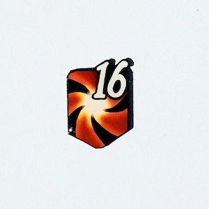 May include: A black and orange swirl design with a white number 16 in the center. The design is on a small, square-shaped object.