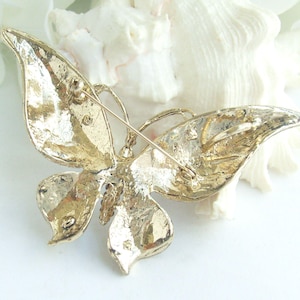 May include: A gold-toned butterfly brooch with textured wings and a pin closure. The butterfly design features detailed veining and a three-dimensional appearance. The brooch is likely made of metal and is suitable for adding to clothing or accessories.