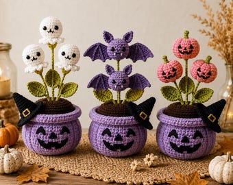 May include: Three crocheted potted plants featuring Halloween themes. The pots are light purple with black jack-o'-lantern faces and small black witch hats. The plants include white ghosts, purple bats, and pink pumpkins on green stems.