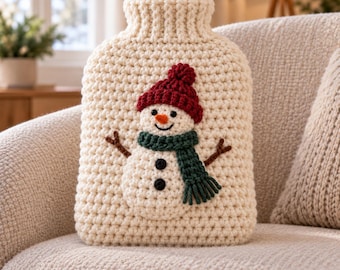 May include: A cream-colored, chunky knit hot water bottle cover featuring a crocheted snowman appliqué. The snowman wears a dark red beanie and a dark green scarf, with brown yarn arms and two black buttons on its body. The cover has a ribbed neck.
