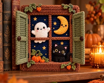 May include: A crocheted window frame display featuring a dark blue night sky background with a white ghost, a yellow crescent moon, a black cat, and orange pumpkins. The frame is brown with sage green shutters and small orange accents.