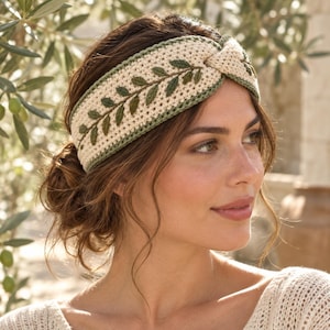 May include: A cream-colored crochet headband featuring a central twisted knot detail and an embroidered olive branch pattern in shades of dark and light green. The headband is finished with a thin green border along the top and bottom edges.