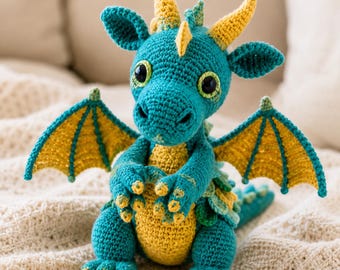 May include: A teal and yellow crocheted dragon plush toy featuring large black safety eyes, two pointed horns on the head, a yellow belly, and two outstretched wings with yellow centers and teal borders, standing on four clawed feet.