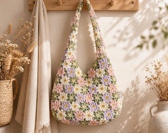May include: A crochet shoulder bag constructed from individual floral motifs in shades of pastel pink, lavender, white, and sage green. The bag features a continuous pattern of interconnected flowers with yellow centers and a single integrated shoulder strap.
