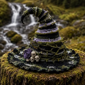 May include: A crocheted witch hat featuring a spiraling design in black, olive green, and lavender yarn. The hat is adorned with a purple crocheted rose and three small white skull figures at the base, with white spiderweb embroidery on the brim.