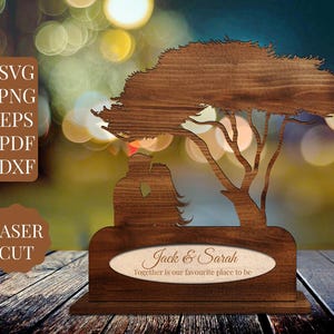May include: A laser-cut wooden sculpture featuring a tree and two figures embracing. The base includes an oval plaque with the names "Jack & Sarah" and the phrase "Together is our favourite place to be." The sculpture is brown with a natural wood grain.