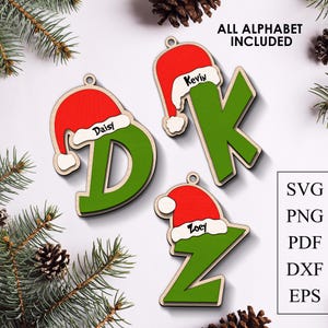 Puede incluir: Adornos navideños de madera con forma de las letras D, K y Z, cada uno pintado de verde y rematado con un gorro de Papá Noel rojo. Los nombres "Daisy", "Kevin" y "Zoey" están escritos en los gorros. El texto "ALL ALPHABET INCLUDED" está en la parte superior.