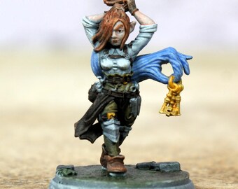 Pode incluir: Figura em miniatura de fantasia de uma elfa, pintada com detalhes. Ela usa uma camisa branca, botas marrons e armadura. Uma mão azul segura uma chave dourada. A figura está em uma base circular cinza.
