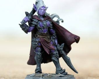 Pode incluir: Uma figura de fantasia em miniatura de uma guerreira com pele roxa, vestindo uma armadura escura e uma capa bordô. Ela segura uma espada e está em uma base cinza. A figura tem orelhas longas e pontudas e cabelo branco, e é pintada com sombreamento detalhado.