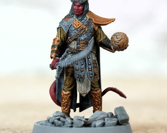 Pode incluir: Figura de fantasia em miniatura de um demônio de pele vermelha com chifres, segurando uma arma de lâmina e um orbe texturizado. A figura usa uma armadura ornamentada em tons de ouro, cinza e marrom, com uma longa cauda e uma capa fluida.