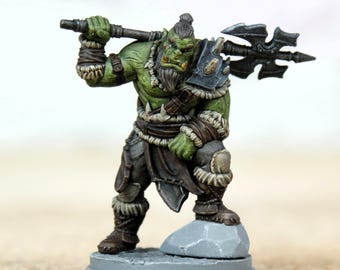 Pode incluir: Uma figura em miniatura de um guerreiro orc de pele verde, segurando um grande machado sobre o ombro. O orc está vestido com uma armadura escura e roupas com bordas de pele, em pé sobre uma pequena base de pedra. A figura é pintada com sombreamento detalhado.