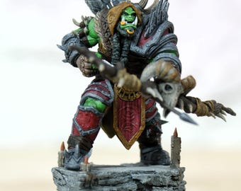 Pode incluir: Figura em miniatura detalhada de um guerreiro orc de fantasia, posando com arco e flecha. O orc tem pele verde, armadura vermelha e cinza e um capacete com chifres. A figura é montada em uma base de pedra com caveiras.