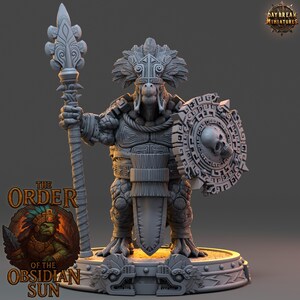 Può includere: Una statuetta in miniatura grigia di un guerriero con lancia e scudo. Il guerriero indossa un'armatura ornata e un copricapo di piume. Lo scudo presenta un teschio. La base della statuetta riporta la scritta "THE ORDER OF THE OBSIDIAN SUN".