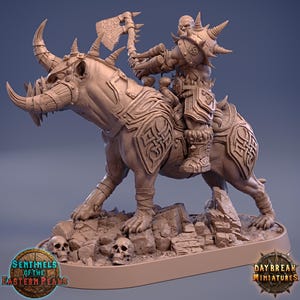 May include: A detailed miniature sculpture of a warrior riding a horned beast, wielding an axe. The sculpture is a light brown color and sits on a base with skulls and rock formations. The sculpture has intricate armor and weapon details. Logos for "Sentinels of the Eastern Peaks" and "Daybreak Miniatures" are visible.
