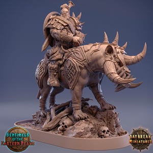 May include: A detailed, beige miniature sculpture of a warrior riding a horned beast. The warrior is clad in ornate armor, and the beast has tusks and a skull-like head. The base features skulls and the text "Sentinels of the Eastern Peaks" and "Daybreak Miniatures".