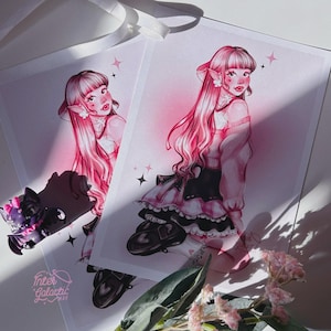Può includere: Due stampe artistiche raffiguranti un personaggio con capelli rosa e orecchie a punta, vestito con un abito rosa e nero. Le stampe sono su carta bianca, con un accessorio a forma di gatto nero e il testo "Inter Galactic Wax".