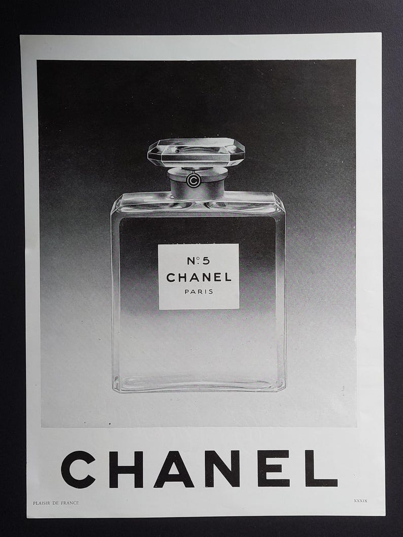 Puede incluir: Anuncio en blanco y negro de perfume Chanel N&deg;5. La imagen muestra un frasco de perfume transparente y rectangular con un tap&oacute;n facetado. La etiqueta dice "N&deg;5 CHANEL PARIS". El logotipo de CHANEL est&aacute; en la parte inferior.