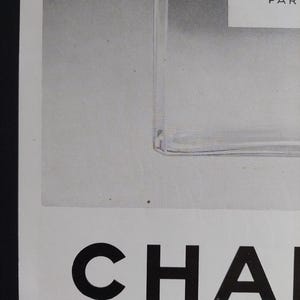 Puede incluir: Anuncio en blanco y negro con un frasco de perfume y la palabra "CHANEL" en negrita. Tambi&eacute;n se ve el texto "N:5" y "PAR". La frase "PLAISIR DE FRANCE" est&aacute; impresa en la parte inferior.