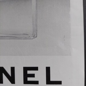 Puede incluir: Un anuncio en blanco y negro con un frasco de perfume y la palabra "NEL" en letras may&uacute;sculas negras y en negrita. La botella es parcialmente visible, con una etiqueta blanca. El n&uacute;mero romano "XXXIX" est&aacute; en la esquina inferior derecha.