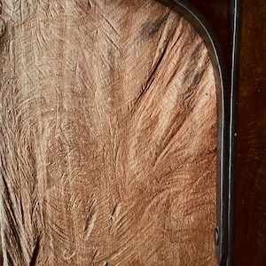May include: A dark metal shelf bracket with a curved design. The bracket is mounted on a textured, brown wooden surface. The bracket is a right angle shape, with a flat top and a vertical support.