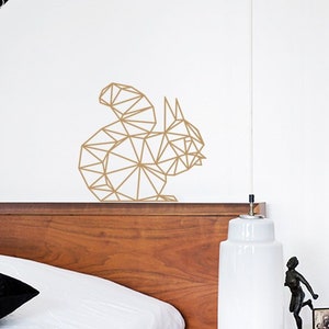 May include: Geometric gold squirrel wall decal on a white wall above a wooden headboard and a white bedside lamp.