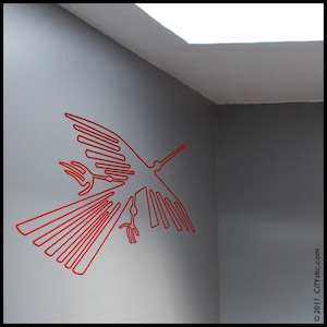 May include: A red line art design of a bird in flight, applied to a gray wall. The bird's wings are spread, and its beak is pointed forward. The design is a minimalist, modern style.