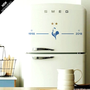 Puede incluir: Un refrigerador blanco con un gallo azul y dos estrellas doradas en la parte delantera. El refrigerador tiene la palabra "SMEG" escrita en la parte superior y los a&ntilde;os "1998" y "2018" en la parte inferior.