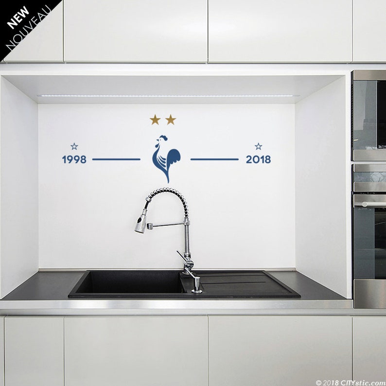 Puede incluir: Un salpicadero de cocina blanco con un gallo azul y dos estrellas doradas. El gallo est&aacute; centrado entre los a&ntilde;os 1998 y 2018, que est&aacute;n escritos a ambos lados del gallo.