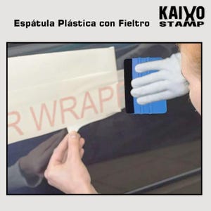 Puede incluir: Una espátula de plástico azul con borde negro se utiliza para aplicar una envoltura de vinilo. La palabra "WRAP" es parcialmente visible en el vinilo. La imagen también muestra el texto "Espátula Plástica con Fieltro" y "KAIXO STAMP".