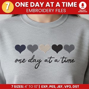 Puede incluir: Una sudadera gris claro con corazones bordados en azul marino, gris, beige, negro y gris. La frase "one day at a time" está bordada debajo de los corazones. La imagen también incluye el texto "ONE DAY AT A TIME EMBROIDERY FILES".