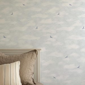 May include: A bedroom scene featuring a white headboard, brown pillows, and a striped pillow. The background is a light blue wallpaper with a cloud and bird pattern. The bedding is a neutral color, creating a calming atmosphere.